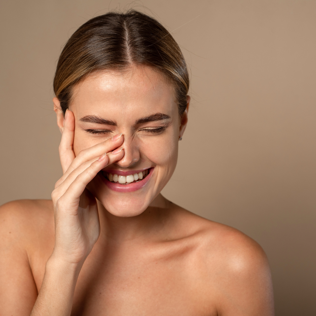 A pretty woman with tanned skin. Her hair is tied back, and she has a hand over half of her face. She's laughing happily