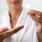 A woman appliesBeau Bronzage Face Drops with Hyaluronic Acid to her hand using the bottle's pipette